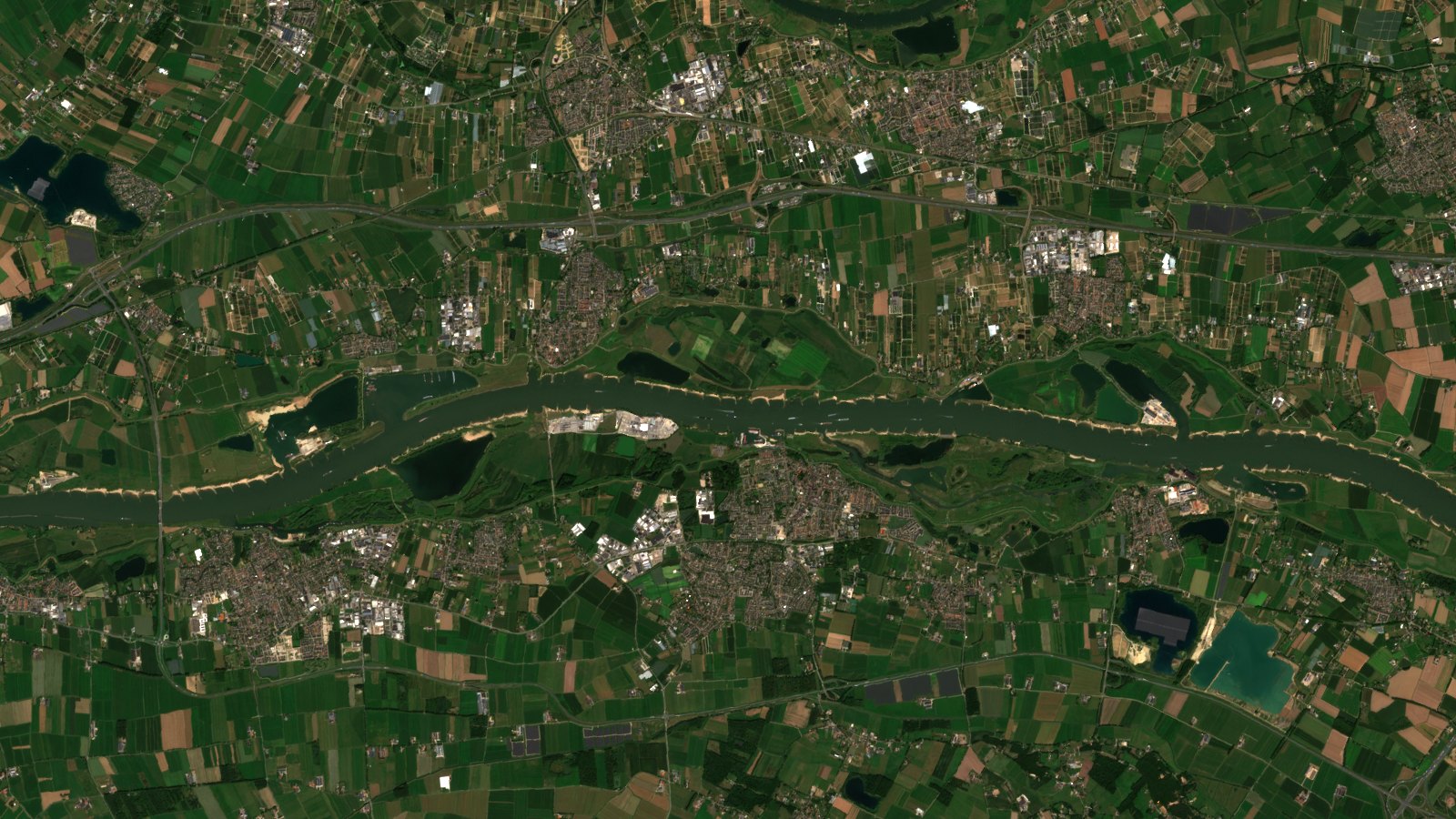El mismo tramo del Waal el 11 de agosto de 2025, en la misma escala y con el mismo procesado. El río forma una cinta ancha y continua de agua oscura, y la franja de arena clara de las orillas es un hilo fino, muy lejos del peine ancho de la escena de 2026.